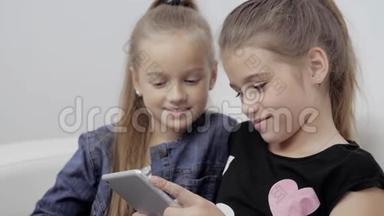 两个微笑的女孩躺在沙发上，用平板电脑，非常快乐的小学生的特写照片